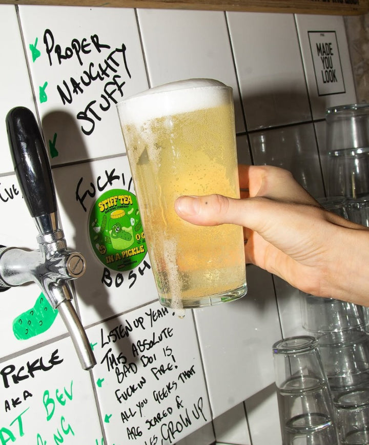 Person holding a glass of beer with a tap handle and text on the wall in the background
