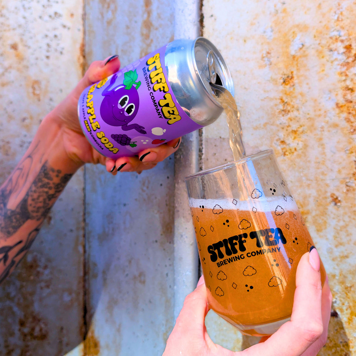 Person pouring Stiff Tea from a can into a glass with the same branding against a textured wall.