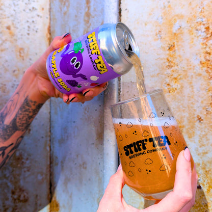 Person pouring Stiff Tea from a can into a glass with the same branding against a textured wall.